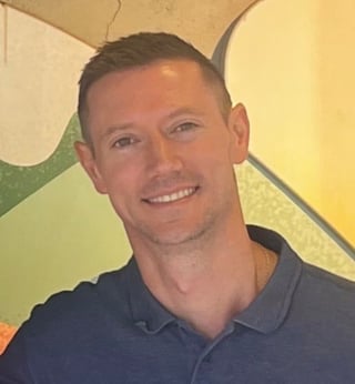 Smiling man in dark blue polo shirt against colorful geometric background with green and yellow tones