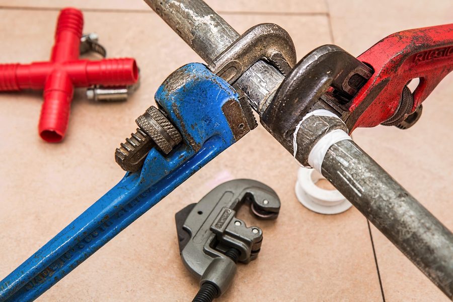 Pipe wrenches, pipe cutter, and fittings laid out on site